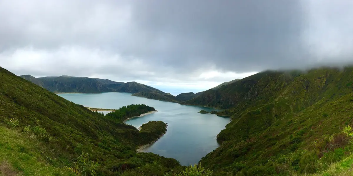 Crater lake in a deep green volcanic valley under a cloudy sky