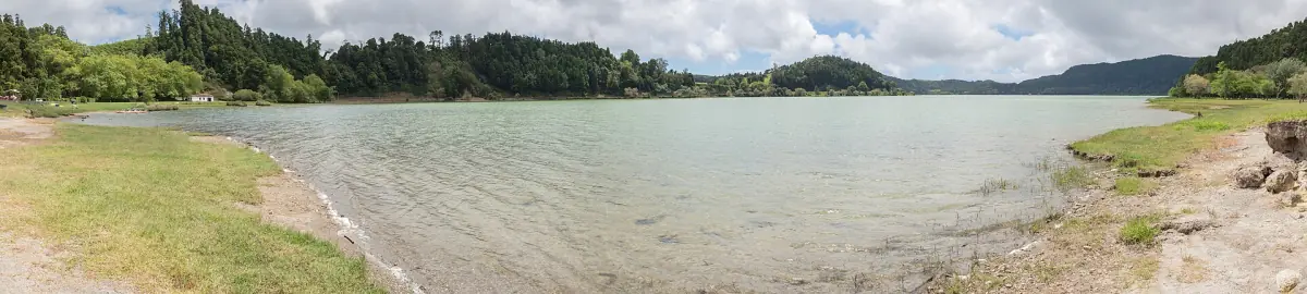 Wide panorama of the calm shore of Furnas lake under a pale sky