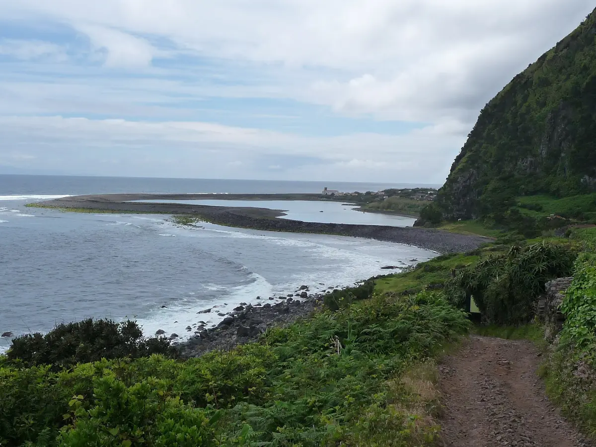 Hiking trail along a green cliff above a dark beach on São Jorge