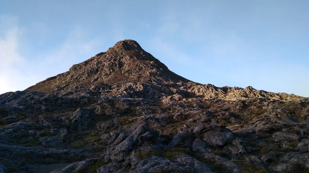 Dark volcanic summit cone of Pico mountain under a blue sky